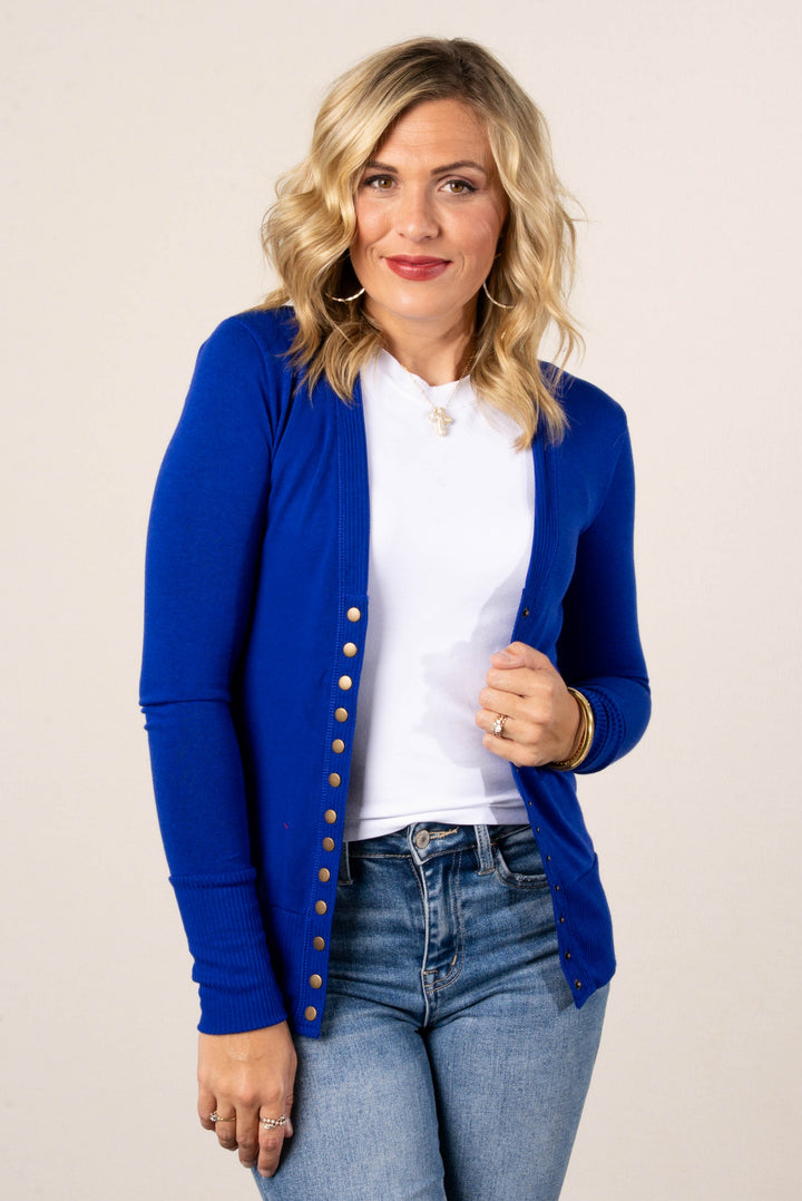 Smiling woman wearing a cobalt blue button-front cardigan over a white t-shirt, styled with high-waisted light wash jeans.