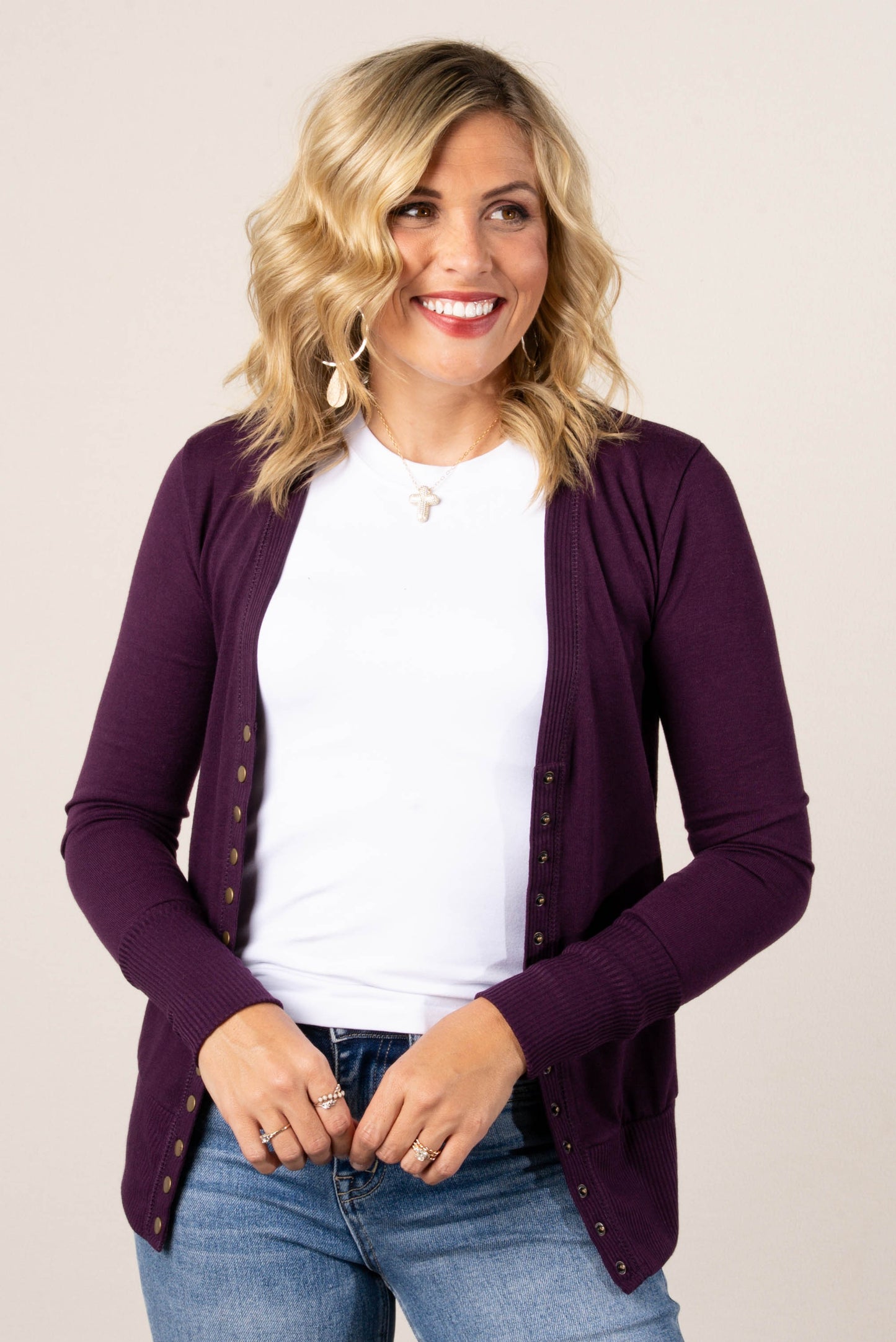 Smiling woman wearing an eggplant colored, button-front cardigan over a white t-shirt, styled with high-waisted light wash jeans.