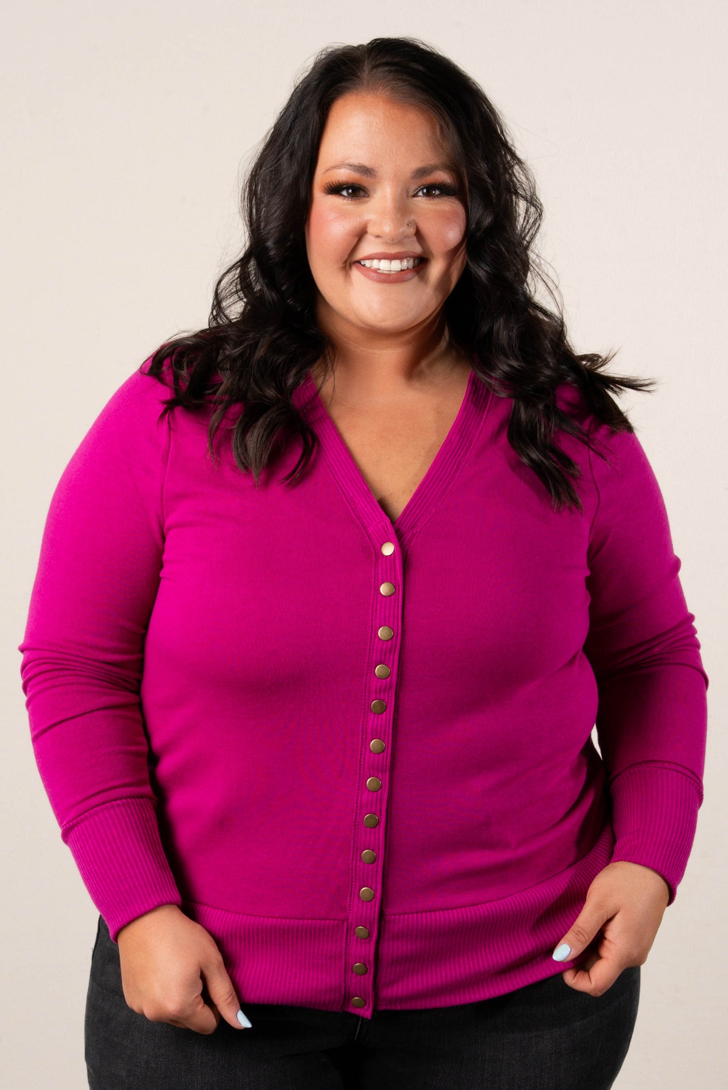 Smiling, plus size woman wearing a magenta button-front cardigan, styled with high-waisted black jeans.