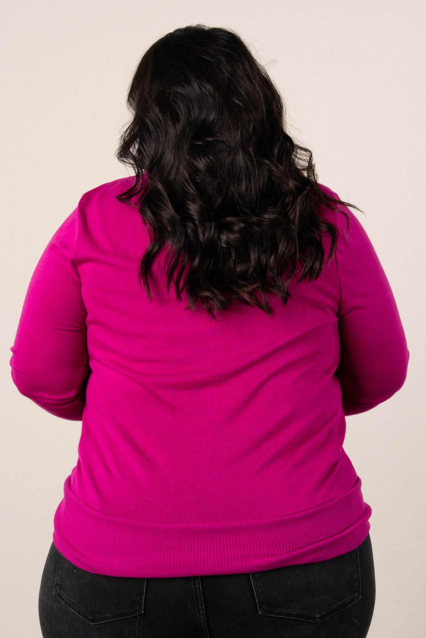 Back of a plus size woman wearing a magenta cardigan, styled with high-waisted black jeans.