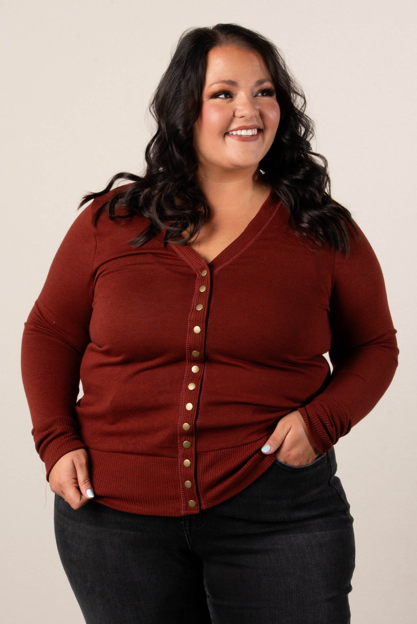 Smiling plus size woman wearing a rust colored, button-front cardigan, styled with high-waisted black jeans.