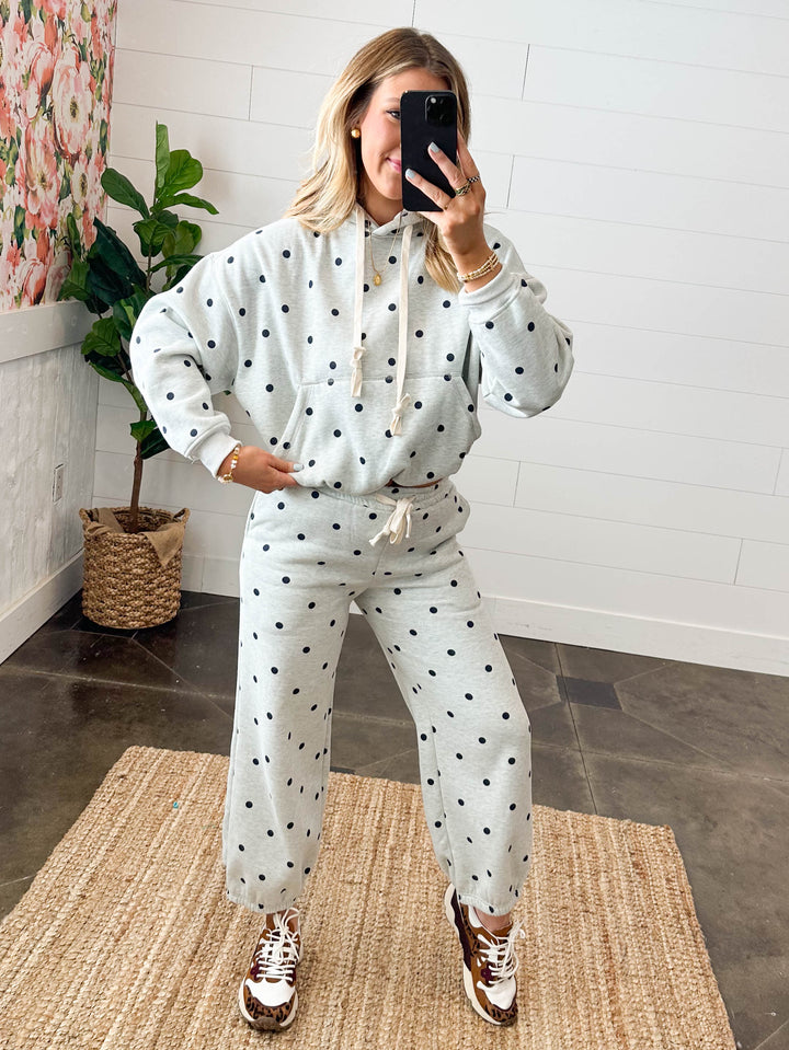 Person wearing a polka dot outfit taking a mirror selfie in a room with a floral painting and plant.