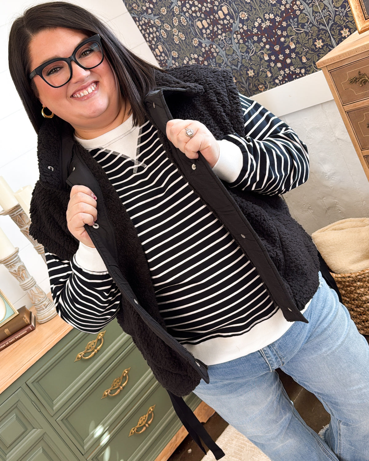 Woman wearing the black sherpa vest open over a black and white striped top