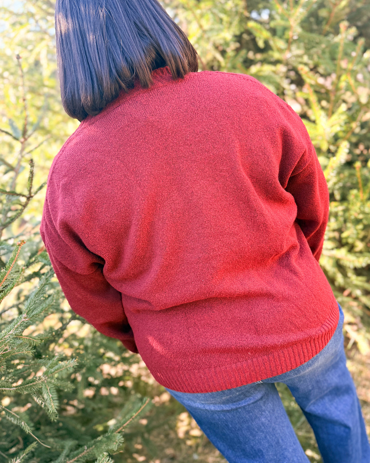 Back view of a red knit sweater styled with medium wash jeans