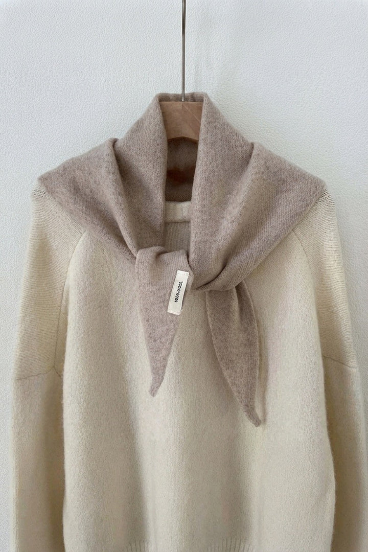 Oatmeal triangle knit scarf tied around the shoulders of a cream sweater on a hanger