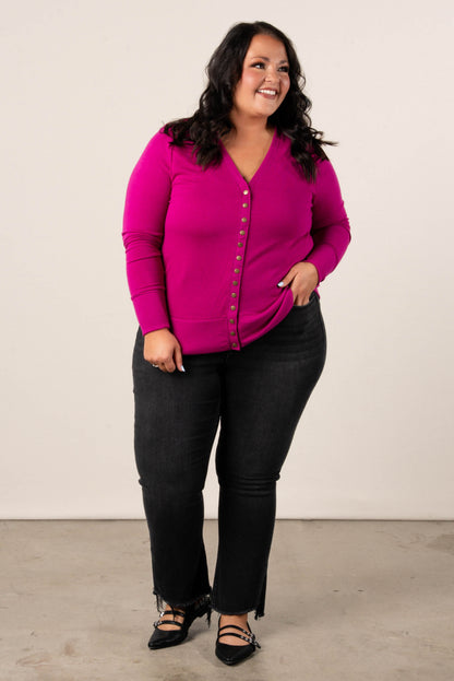Smiling, plus size woman wearing a magenta button-front cardigan, styled with  high-waisted black jeans and black pointed dress flats.