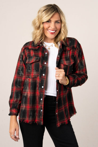 A woman with blonde hair smiling while wearing an open red and black distressed plaid button-down shirt. The shirt has two front pockets with buttons. She is wearing it over a white top and black jeans.