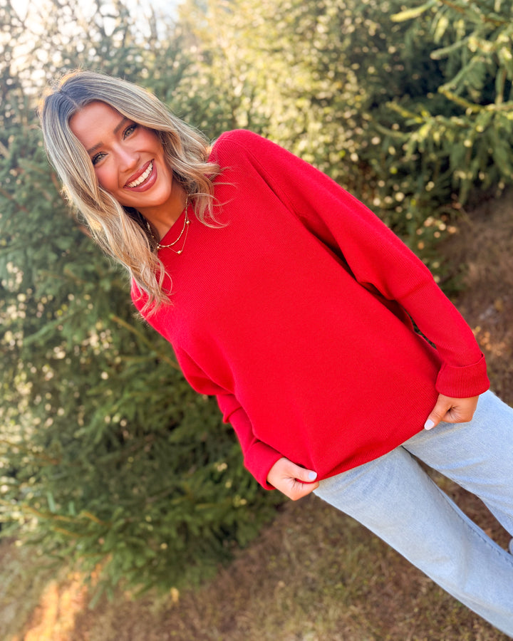 Woman wearing a red ribbed batwing sleeve sweater with light wash jeans