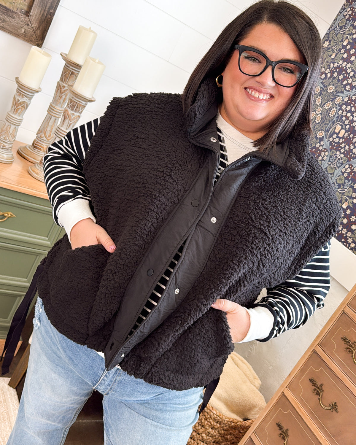 Woman wearing a black oversized sherpa vest over a striped top with light wash jeans