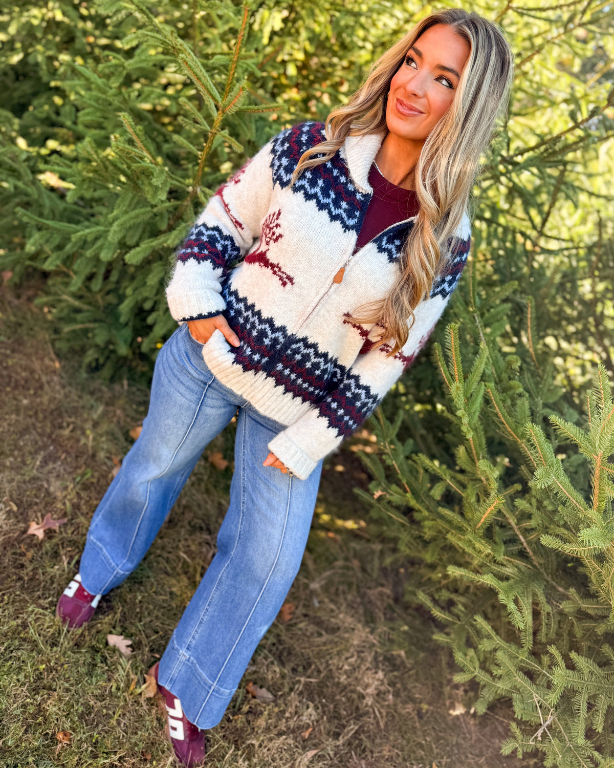 Full-length view of a cream reindeer fair isle sweater cardigan styled with light wash jeans and burgundy sneakers