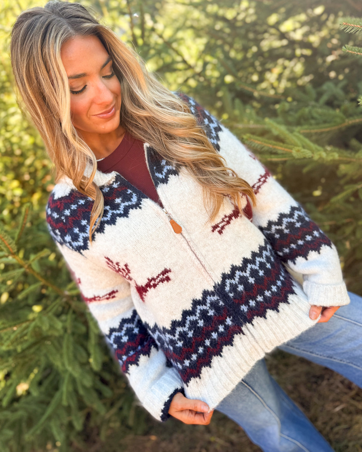Woman wearing a cream fair isle sweater cardigan with navy patterned bands and red reindeer over a burgundy top
