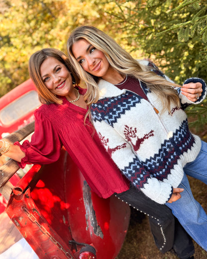 Woman wearing a cream reindeer fair isle sweater cardigan next to a woman in a burgundy blouse