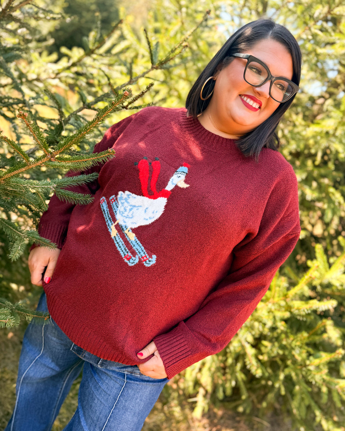 Woman wearing a red knit sweater with a white duck on skis wearing a red scarf styled with jeans