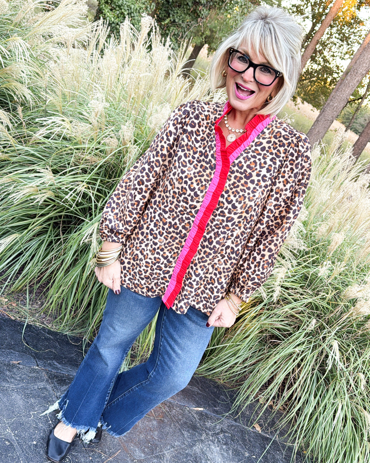 Full-length view of a taupe leopard blouse with red contrast ruffle placket, styled with flare jeans