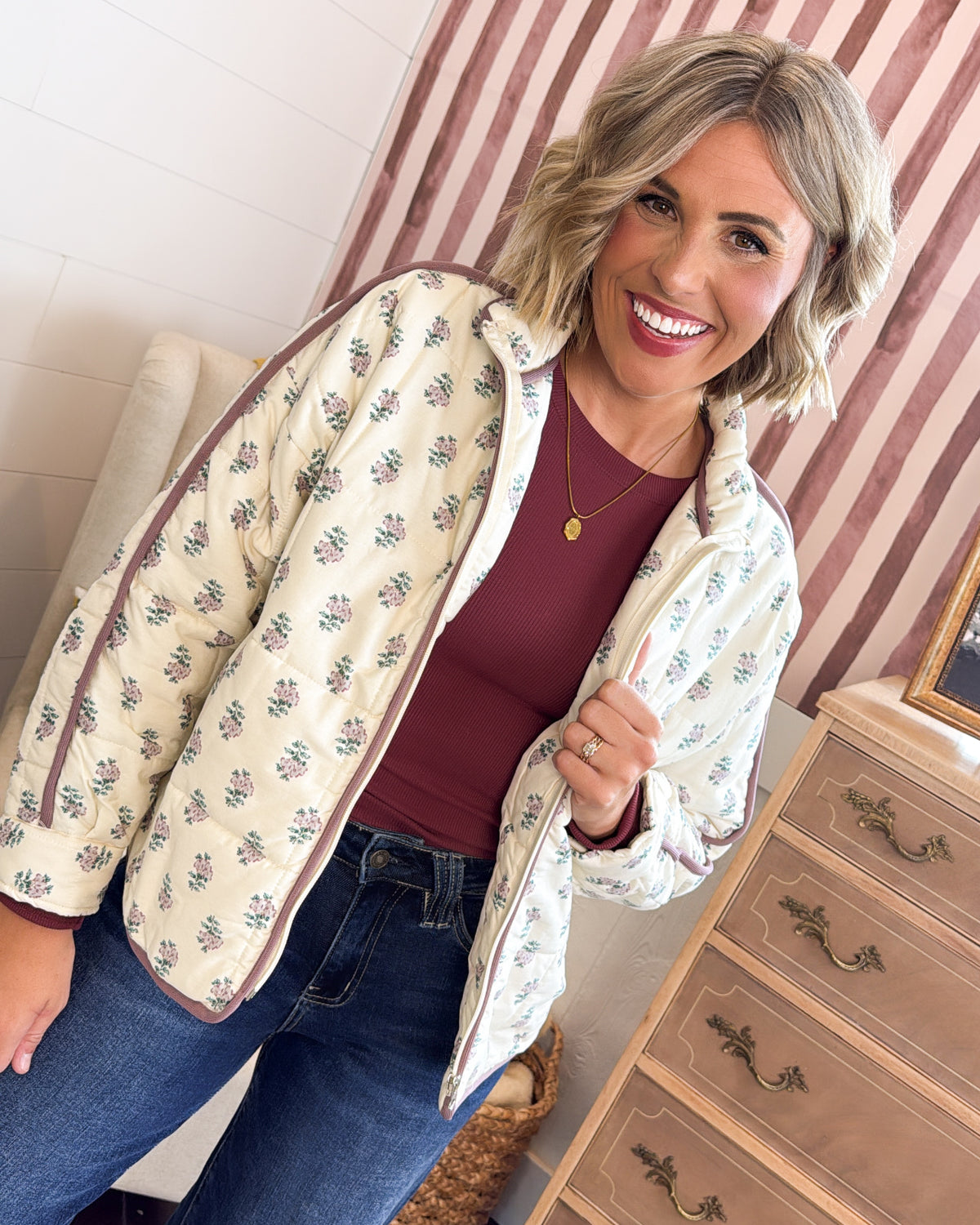 Woman wearing an ecru floral quilted jacket with mauve piping over a burgundy top, styled with dark jeans