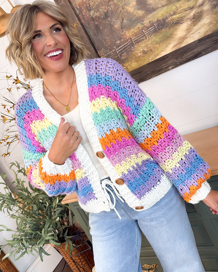 Woman wearing a chunky crochet cardigan with lavender, pink, blue, mint, yellow, and orange stripes and ivory trim