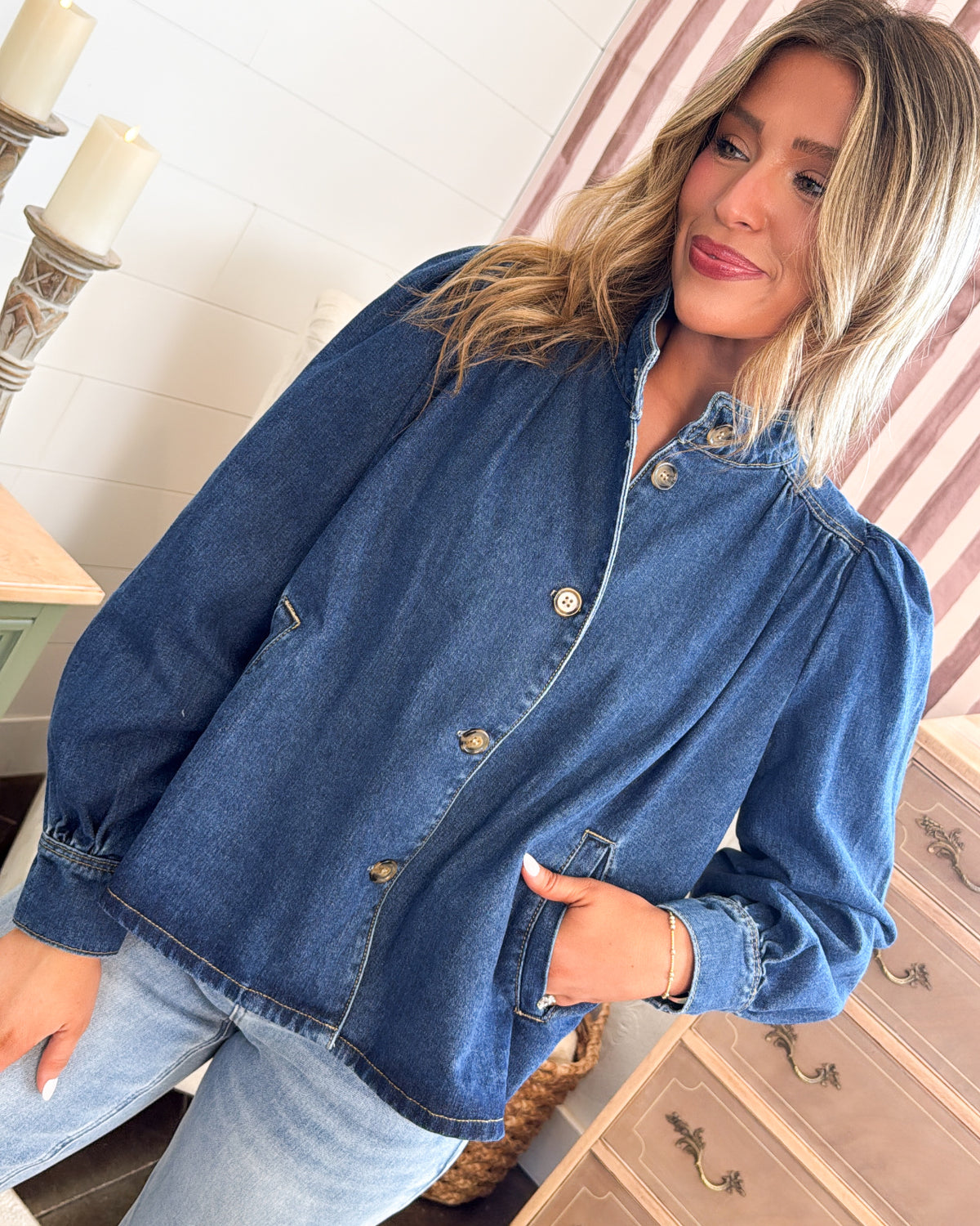 Front view of the medium wash pleated denim jacket with button cuffs and hand in pocket