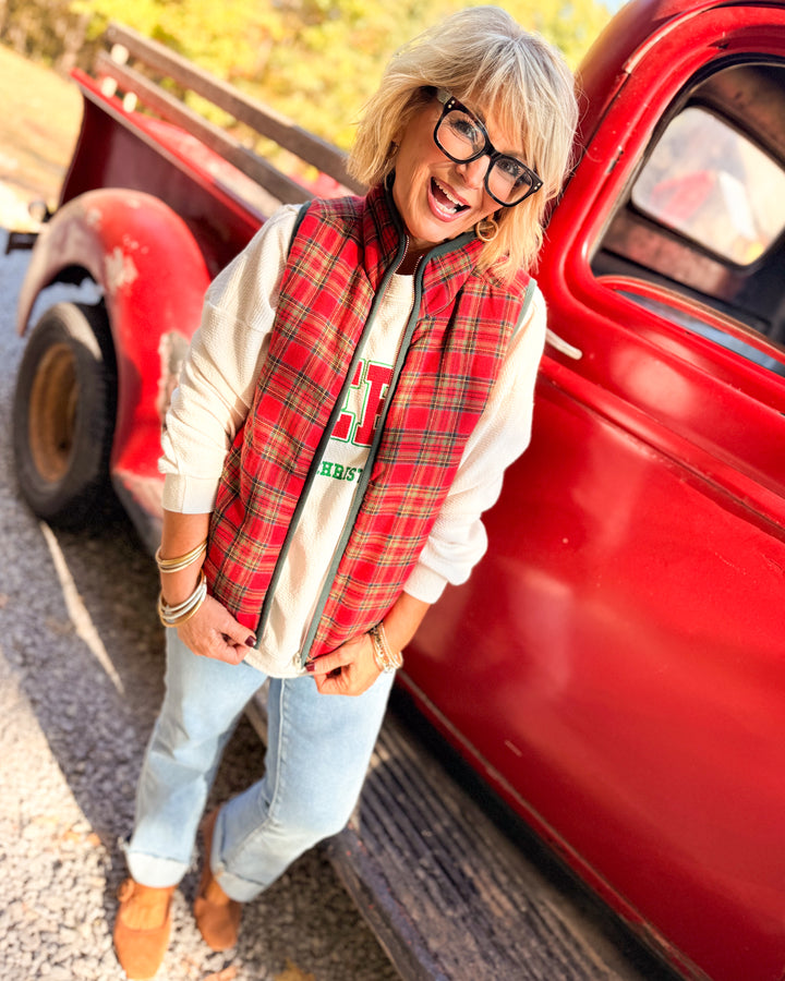 Woman wearing a red plaid flannel vest over a white top styled with light wash jeans